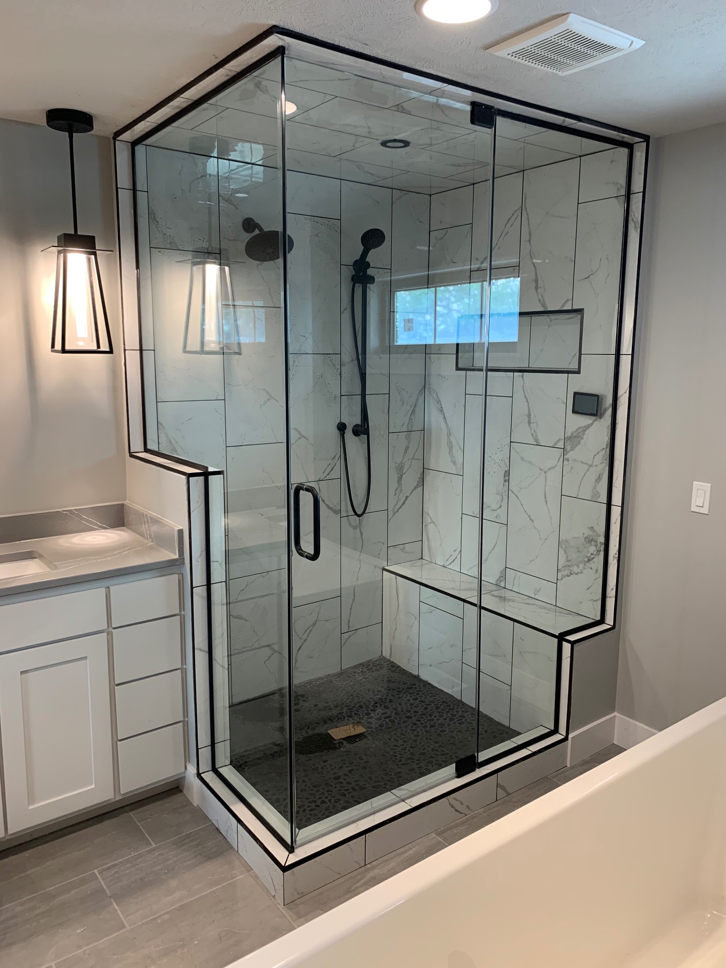 Custom frameless corner shower enclosure with matte black hardware and marble-look tile, installed in an Omaha bathroom