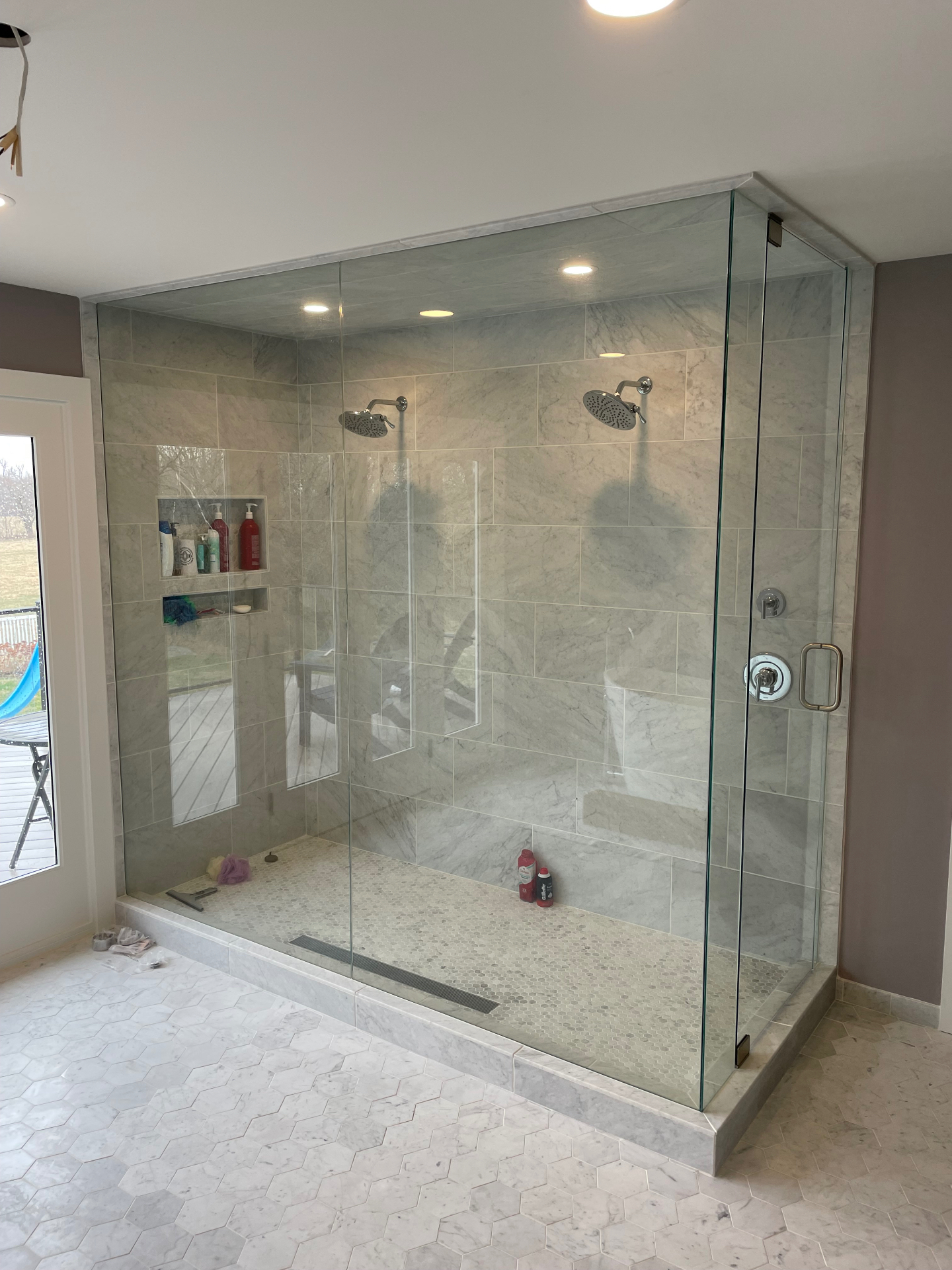 Large frameless shower enclosure with a swing door and fixed panels in a marble tiled bathroom with two shower heads